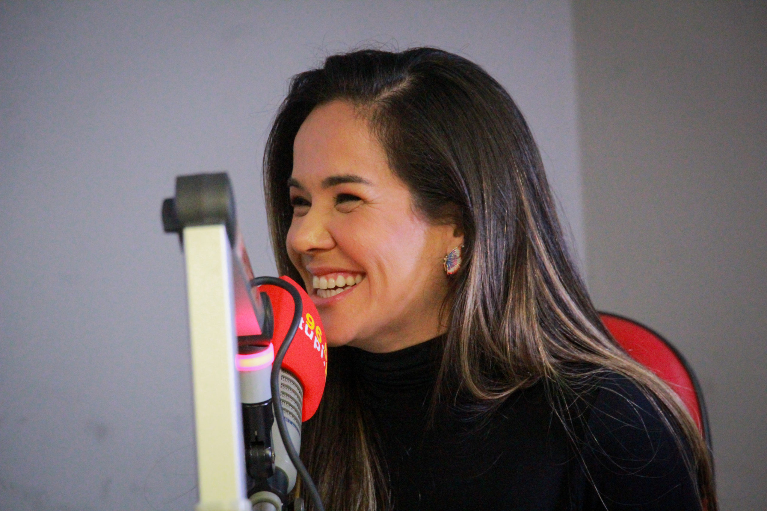isabele benito de blusa preta sorrindo em frente ao microfone da super rádio tupi