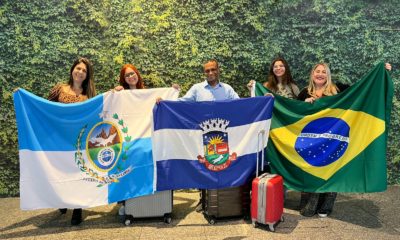 estudantes e professores do Colégio Estadual Marechal Zenóbio sorrindo com as bandeiras do Estado do Rio de Janeiro, da cidade de Nilópolis e do Brasil