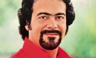 Close-up de Lindomar Castilho sorrindo, com cabelo escuro cacheado, monocelha e barba estilo cavanhaque.