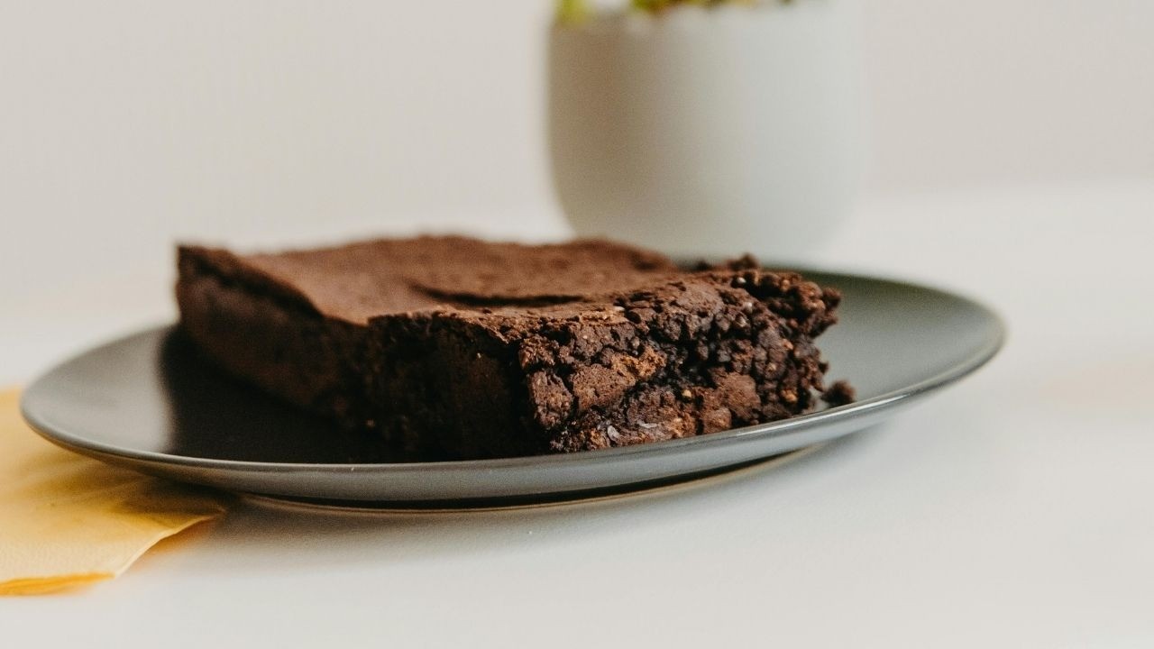 Pedaço de brownie de chocolate em prato cinza escuro, com guardanapo amarelo.