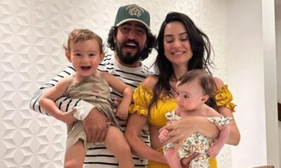 Homem e mulher sorridentes seguram dois filhos pequenos em foto de família.