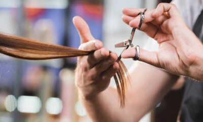 Close-up de mãos de cabeleireiro cortando mecha de cabelo castanho com tesoura prateada.