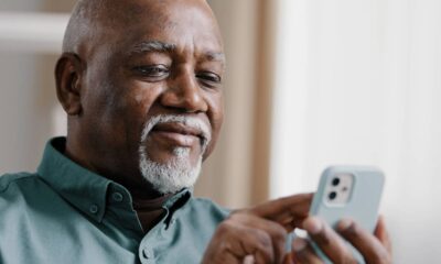 Homem idoso negro de barba branca olhando e usando um smartphone azul claro.