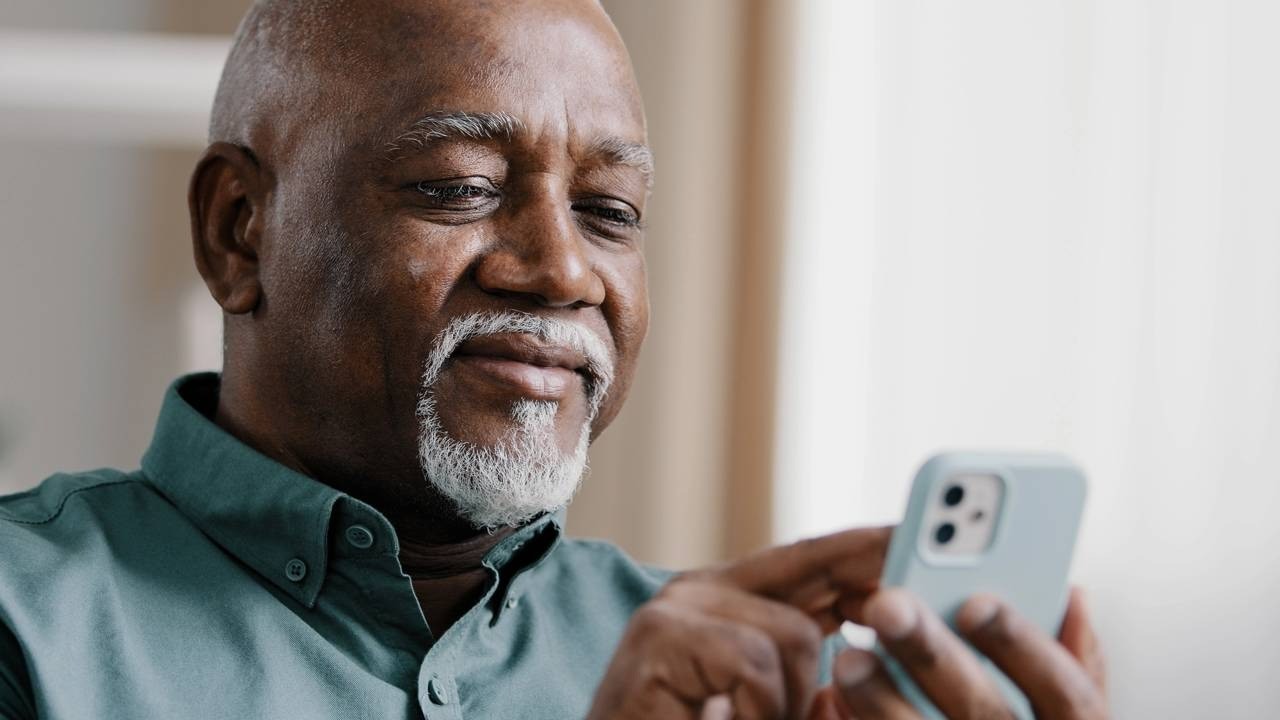 Homem idoso negro de barba branca olhando e usando um smartphone azul claro.