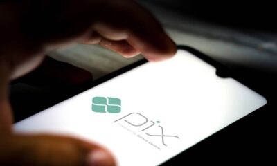 Mão segurando smartphone com o logo do Pix e o texto 'powered by Banco Central' na tela.