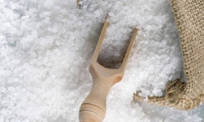 Close-up de cristais de sal branco granulado com uma pequena pá de madeira e um saco de estopa.
