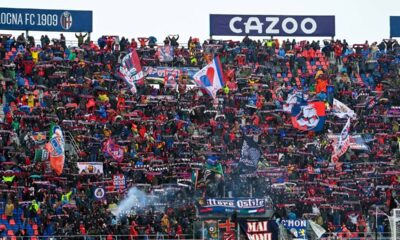 Multidão de torcedores do Bologna no estádio, com bandeiras e cachecóis vermelhos e azuis.