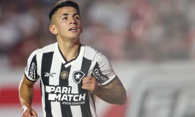 Jogador de futebol do Botafogo em campo com camisa preta e branca, olhando para cima.