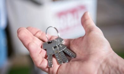 Mão segurando um molho de chaves metálicas em um anel, com fundo claro desfocado.