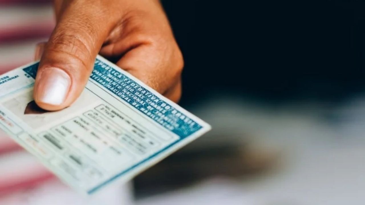 Mão segura Carteira Nacional de Habilitação (CNH) brasileira com fundo escuro.