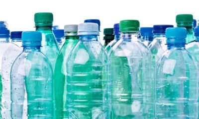 Close-up de muitas garrafas de plástico transparentes e azul-esverdeadas com tampas coloridas em fundo branco.