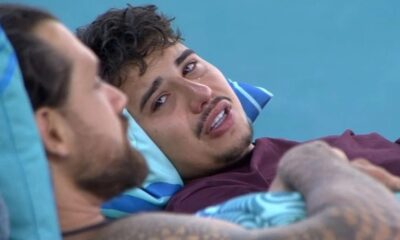 Homem jovem deitado em travesseiro azul, chorando visivelmente, com outro homem ao lado.