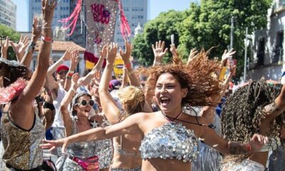 Mulher alegre de cabelo ruivo e top de lantejoulas dança em bloco de Carnaval lotado.