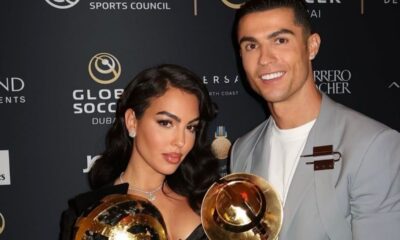 Georgina Rodríguez e Cristiano Ronaldo sorrindo, segurando troféus dourados, em evento Global Soccer.
