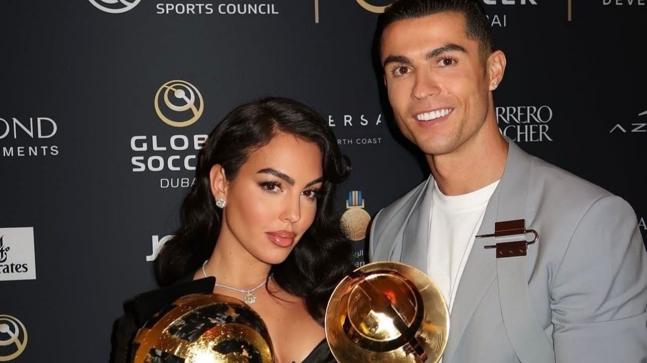 Georgina Rodríguez e Cristiano Ronaldo sorrindo, segurando troféus dourados, em evento Global Soccer.