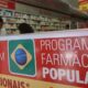 Sinal 'Aqui Tem Farmácia Popular' e 'Anticoncepcionais' em balcão de drogaria com funcionário ao fundo.
