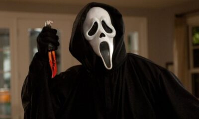 Ghostface com máscara branca e capa preta, segurando faca ensanguentada.