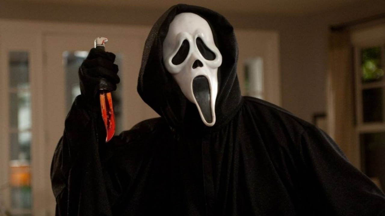 Ghostface com máscara branca e capa preta, segurando faca ensanguentada.
