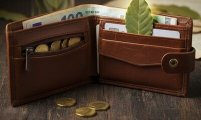 Carteira de couro marrom aberta com notas de euro, moedas e uma folha de louro.