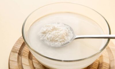 Arroz branco cru de molho em tigela de vidro com água turva e uma colher de metal.