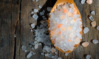 Colher de madeira com sal grosso branco e rosa sobre tábuas de madeira rústicas, sob luz.