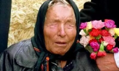 Retrato de Baba Vanga, mulher idosa com lenço na cabeça e olhos fechados, segurando flores coloridas.