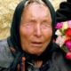Retrato de Baba Vanga, mulher idosa com lenço na cabeça e olhos fechados, segurando flores coloridas.