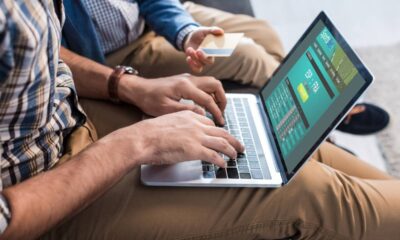 Mãos digitam em laptop exibindo site "SportsBet"; outra mão segura um cartão de crédito.