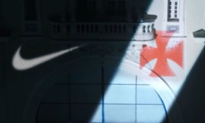 Logo Nike e Cruz de Malta vermelha projetados em fachada de prédio branco, à noite.