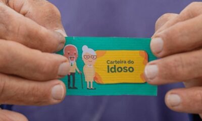 Mãos segurando a Carteira do Idoso, um cartão verde com ilustração de casal de idosos.