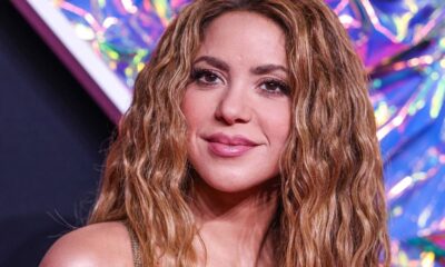 Close-up de Shakira sorrindo, com cabelo ondulado castanho e maquiagem leve.