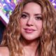 Close-up de Shakira sorrindo, com cabelo ondulado castanho e maquiagem leve.