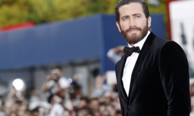 Jake Gyllenhaal, barba, cabelo penteado, veste terno de veludo preto e gravata borboleta em evento.