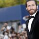 Jake Gyllenhaal, barba, cabelo penteado, veste terno de veludo preto e gravata borboleta em evento.