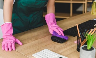 Pessoa com luvas rosas limpa mouse preto em mesa de madeira com pano roxo.