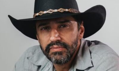 Close-up de homem barbudo usando chapéu de cowboy preto e camisa cinza, olhando para frente.