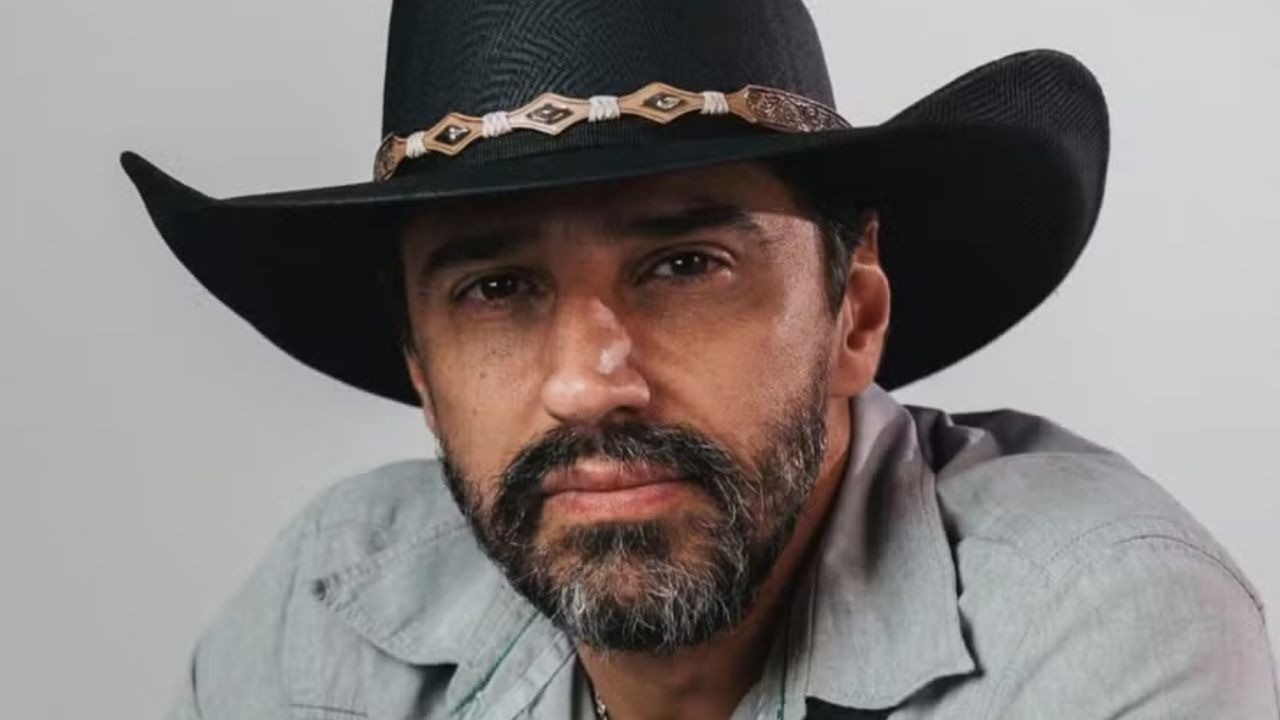 Close-up de homem barbudo usando chapéu de cowboy preto e camisa cinza, olhando para frente.