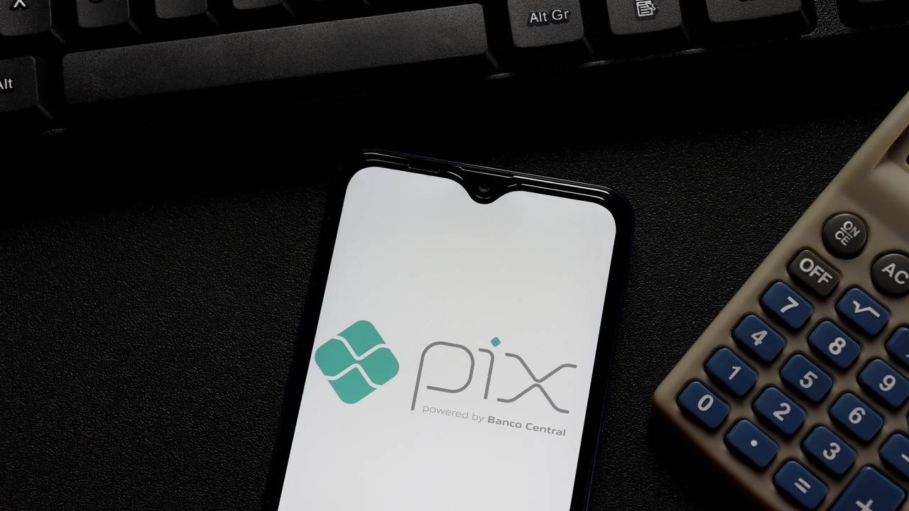 Smartphone com logo Pix e 'powered by Banco Central', teclado e calculadora em superfície escura.
