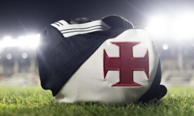 Camisa preta e branca do Vasco da Gama com Cruz de Malta vermelha sobre a grama do estádio.