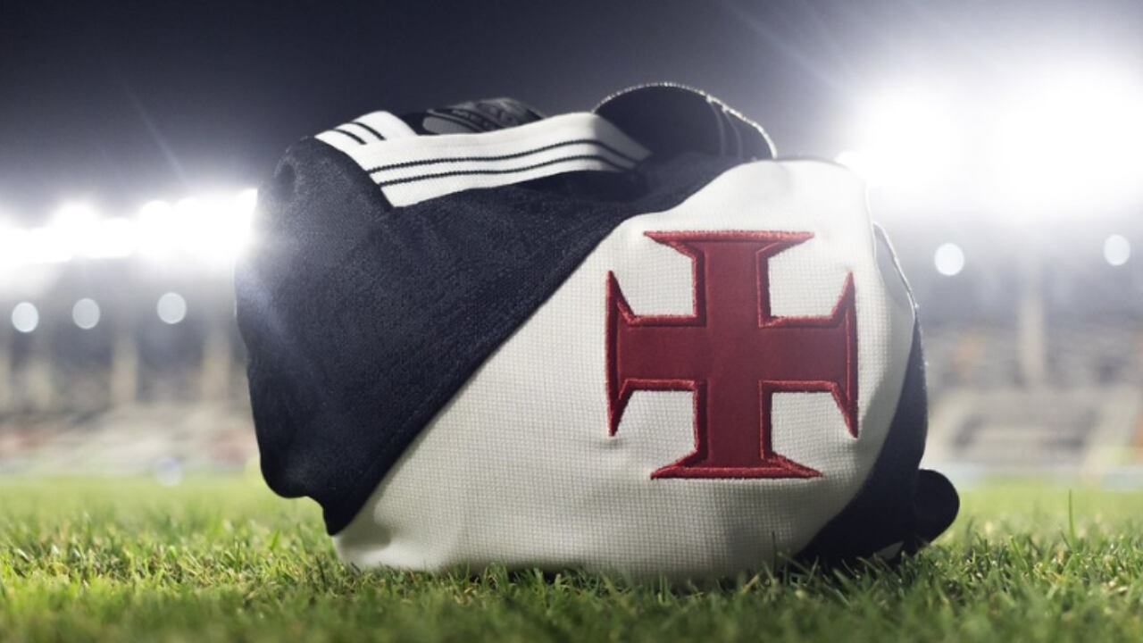 Camisa preta e branca do Vasco da Gama com Cruz de Malta vermelha sobre a grama do estádio.