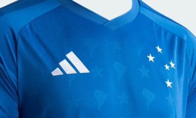 Camisa azul do Cruzeiro com logo Adidas, cinco estrelas brancas e marca d'água de mapas.
