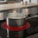 Panela de metal com água fervendo em cooktop de indução preto ligado com brilho vermelho.