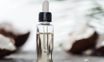 Frasco conta-gotas de óleo com pedaços de coco no fundo desfocado.