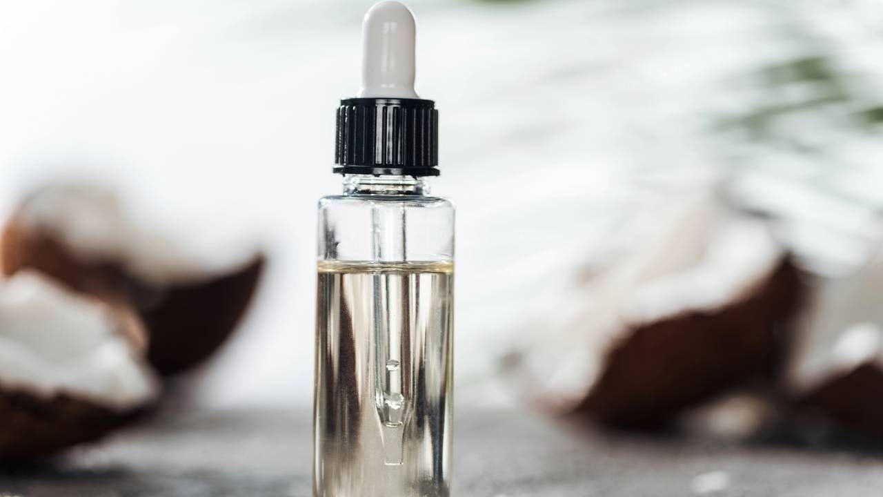 Frasco conta-gotas de óleo com pedaços de coco no fundo desfocado.