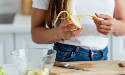 Mãos descascando uma banana sobre uma tábua de corte com uma tigela.