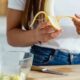 Mãos descascando uma banana sobre uma tábua de corte com uma tigela.
