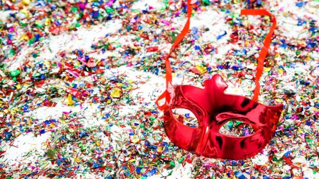 Máscara de carnaval vermelha brilhante sobre fundo de confetes coloridos.