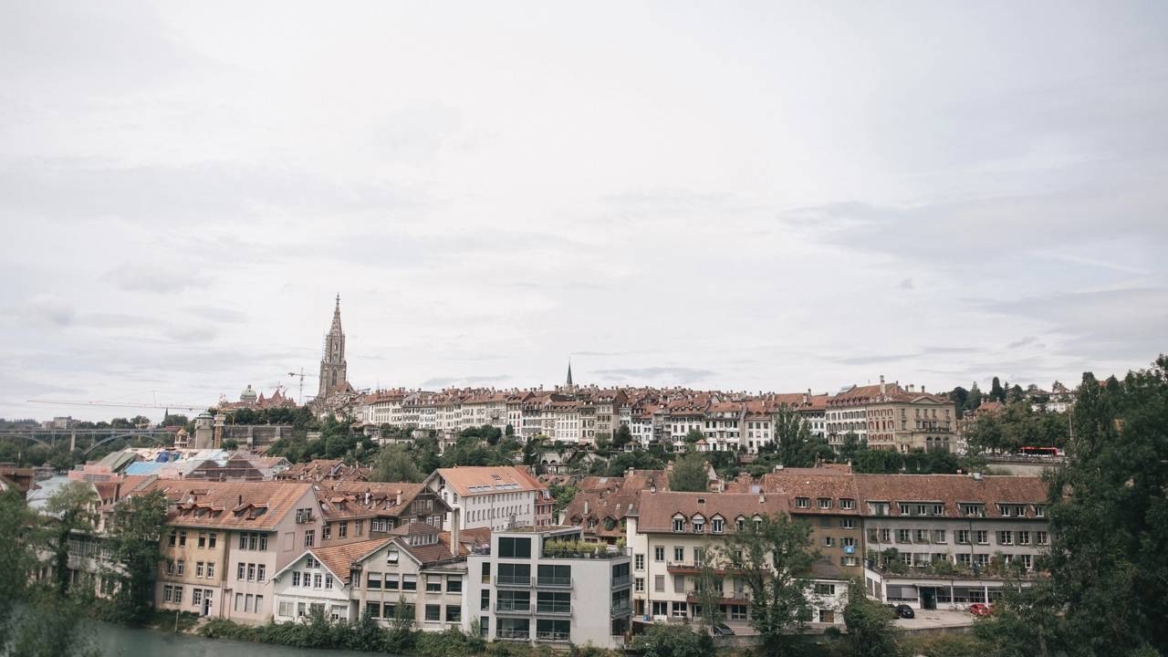 Vista panorâmica de cidade histórica suíça com edifícios de telhado vermelho, rio e torre de igreja.