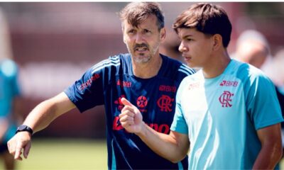 Treinador do Flamengo de camisa azul conversa com jovem jogador de camisa clara em campo.
