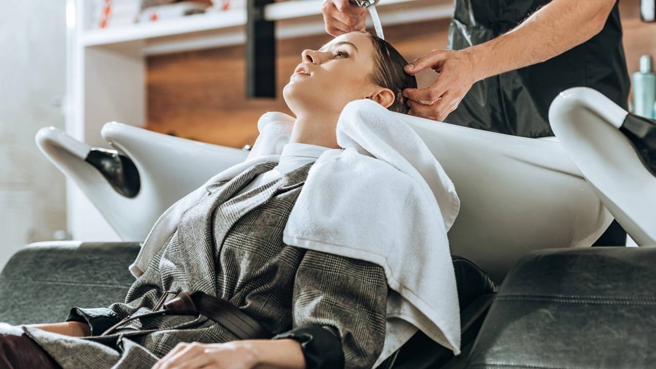 Mulher tem cabelo lavado por cabeleireiro em lavatório branco de salão de beleza.